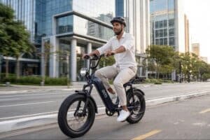 Homem de capacete e roupas claras pilotando uma bicicleta elétrica preta em uma rua urbana com prédios modernos ao fundo.